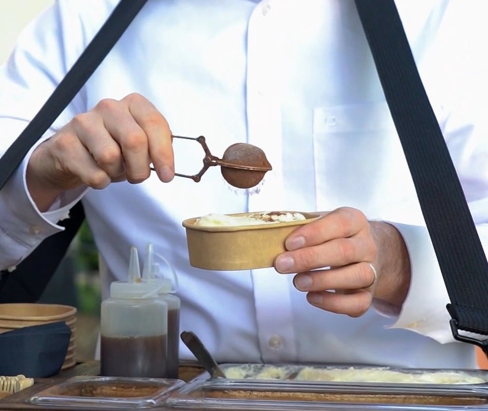 Gijs strooit cacao over een verse portie tiramisu boven het hangende dienblad